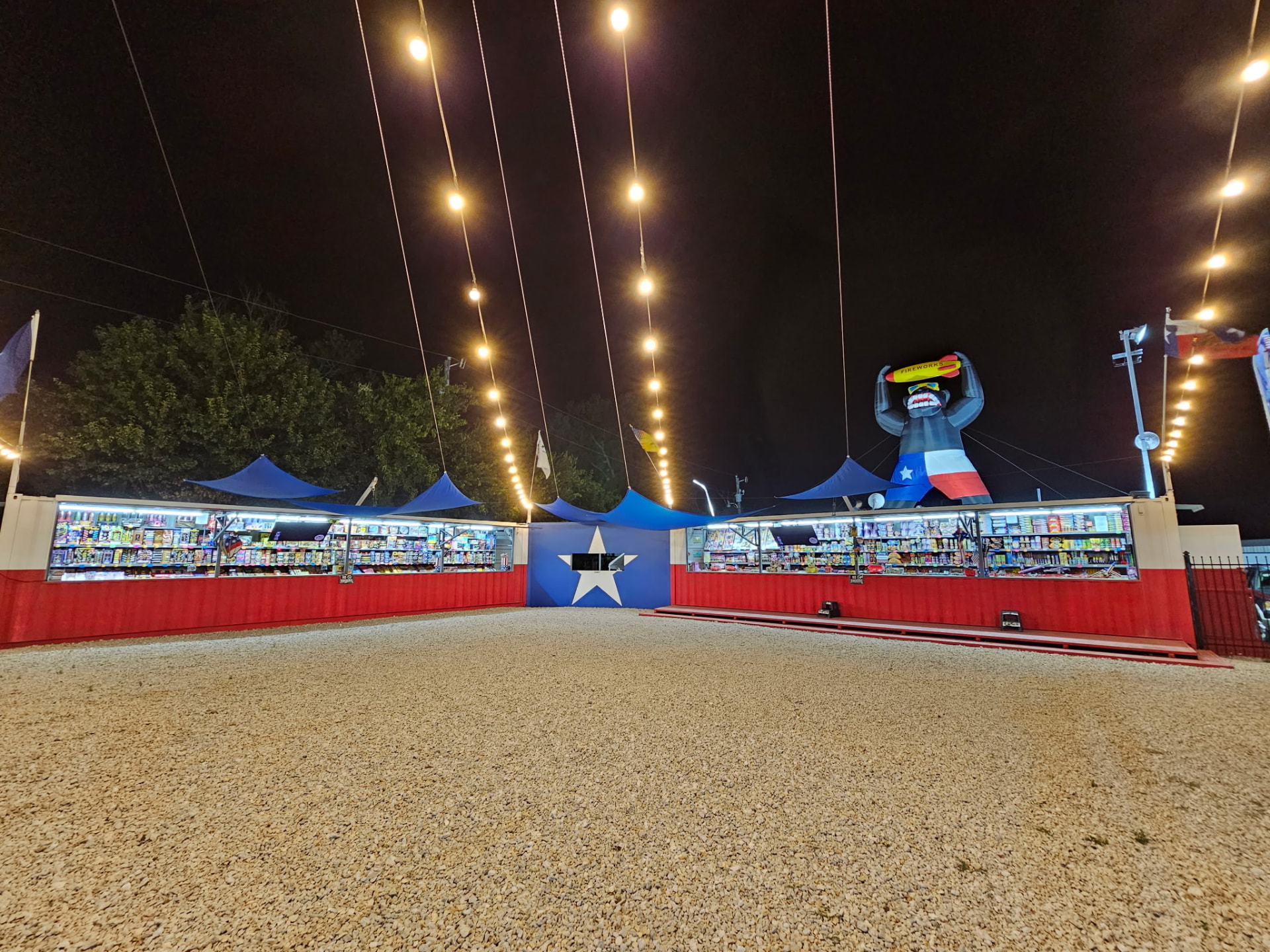 All About Pyrotechnics stand at night, strung with lights beside a painted Texas lone star wall